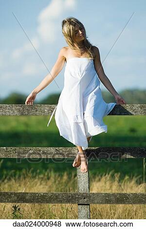 Young woman in dress sitting on rural fence with arms out, eyes closed View Large Photo Image Stock Photo - Young woman in dress sitting on rural fence with arms out, eyes closed. Fotosearch