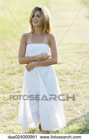 Young woman in dress standing in field, arms folded View Large Photo Image Stock Image - Young woman in dress standing in field, arms folded. Fotosearch