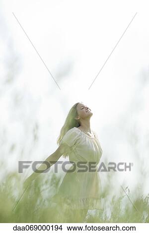 Young woman in field of tall grass, standing with head back and eyes closed View Large Photo Image Picture - Young woman in field of tall grass, standing with head back and eyes closed. Fotosearch