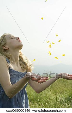 Stock Photograph - Young woman in field, with eyes closed, throwing flower petals in air. Fotosearch