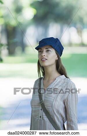 Young woman in park, wearing cap, looking out of frame View Large Photo Image Stock Photo - Young woman in park, wearing cap, looking out of frame. Fotosearch