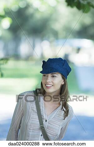 Young woman in park, wearing cap, looking out of frame View Large Photo Image Stock Photo - Young woman in park, wearing cap, looking out of frame. Fotosearch