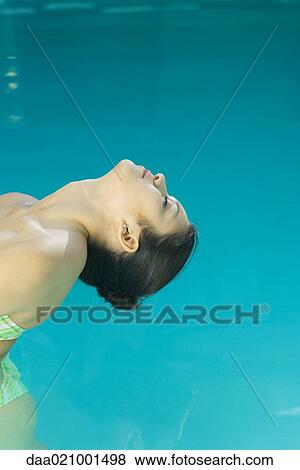 Stock Photo - Young woman in pool, bending head backwards towards water, cropped view. Fotosearch