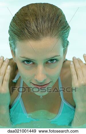 Stock Photo - Young woman in pool, hands by side of face and face dripping. Fotosearch
