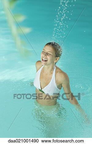 Stock Image - Young woman in pool, standing under stream of water, eyes closed. Fotosearch