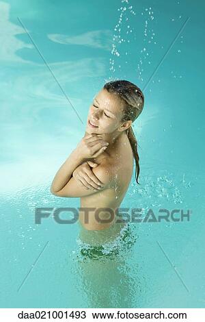 Stock Image - Young woman in pool, standing under stream of water, covering bare chest, eyes closed. Fotosearch