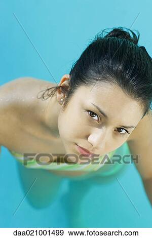Stock Photo - Young woman in pool wearing bikini, looking up at camera, close-up, high angle view. Fotosearch