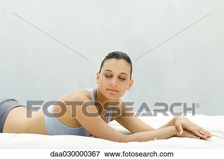 Young woman in sports bra lying on stomach, smiling, eyes closed View Large Photo Image Stock Photo - Young woman in sports bra lying on stomach, smiling, eyes closed. Fotosearch