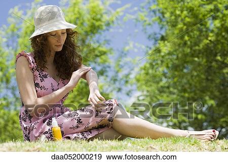 Young woman in sun hat sitting outdoors, applying sunscreen View Large Photo Image Stock Photo - Young woman in sun hat sitting outdoors, applying sunscreen. Fotosearch