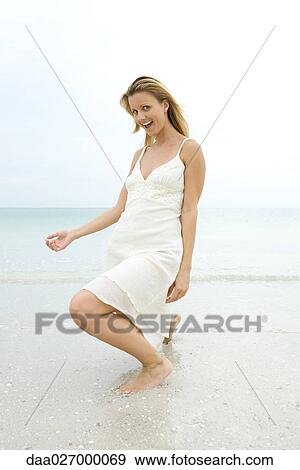 Young woman in sundress crouching in surf, making face at camera View Large Photo Image Stock Photo - Young woman in sundress crouching in surf, making face at camera. Fotosearch