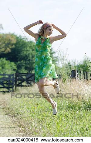 Stock Photography - Young woman in sundress jumping in rural field. Fotosearch
