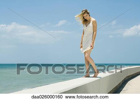 Young woman in sundress standing on low wall by the sea, eyes closed View Large Photo Image Stock Image - Young woman in sundress standing on low wall by the sea, eyes closed. Fotosearch
