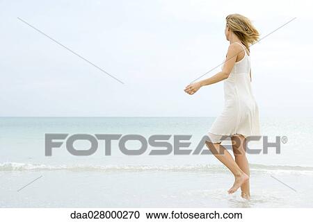 Young woman in sundress walking in shallow water at beach, looking toward horizon View Large Photo Image Stock Image - Young woman in sundress walking in shallow water at beach, looking toward horizon. Fotosearch