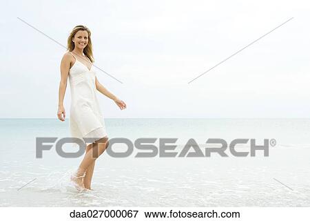 Young woman in sundress walking in shallow water, smiling at camera View Large Photo Image Stock Photo - Young woman in sundress walking in shallow water, smiling at camera. Fotosearch