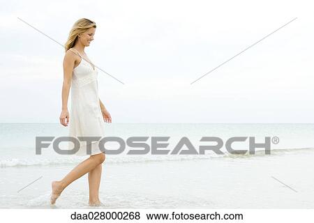 Young woman in sundress walking in surf at beach, smiling, full length View Large Photo Image Stock Photo - Young woman in sundress walking in surf at beach, smiling, full length. Fotosearch