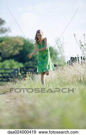 Stock Photo - Young woman in sundress walking through rural field, holding flower. Fotosearch