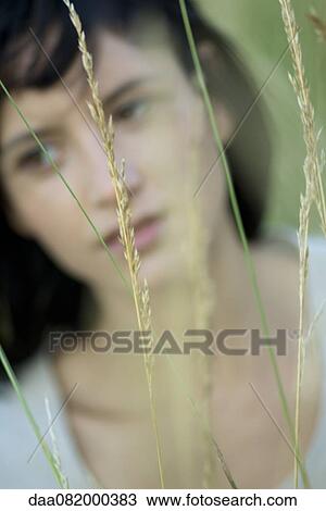 Stock Image - Young woman in tall grass, blurred vegetation in foreground. Fotosearch