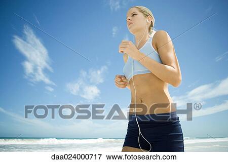 Young woman jogging on beach, listening to MP3 player, low angle view View Large Photo Image Stock Photo - Young woman jogging on beach, listening to MP3 player, low angle view. Fotosearch