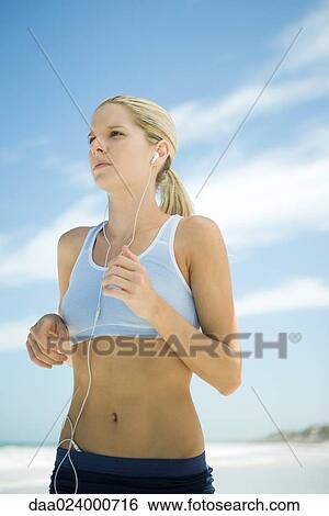 Stock Photograph - Young woman jogging on beach, listening to MP3 player. Fotosearch