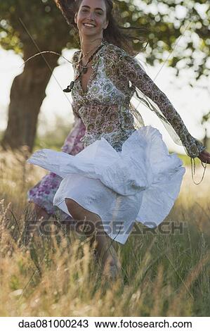 Stock Image - Young woman jumping in field, smiling. Fotosearch