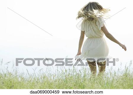 Stock Photo - Young woman jumping in meadow, rear view. Fotosearch