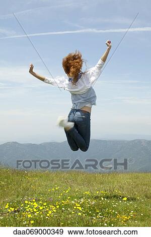 Stock Photo - Young woman jumping in midair outdoors, rear view. Fotosearch