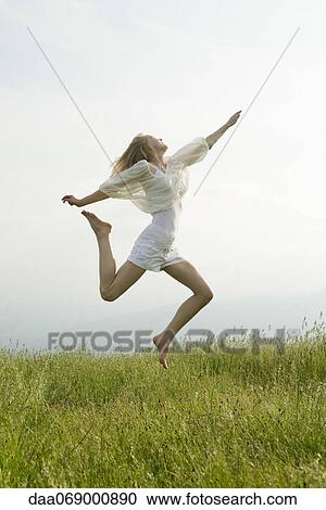 Stock Image - Young woman jumping in midair, side view. Fotosearch