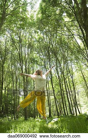 Stock Image - Young woman jumping in woods. Fotosearch