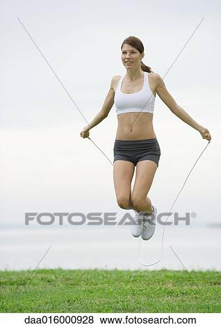 Stock Photo - Young woman jumping rope by lakeside. Fotosearch