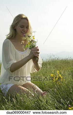 Young woman kneeling in meadow, smelling bouquet of wildflowers View Large Photo Image Stock Photo - Young woman kneeling in meadow, smelling bouquet of wildflowers. Fotosearch