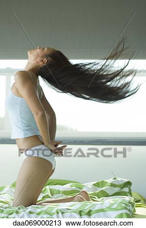 Young woman kneeling on bed tossing hair View Large Photo Image Stock Image - Young woman kneeling on bed tossing hair. Fotosearch