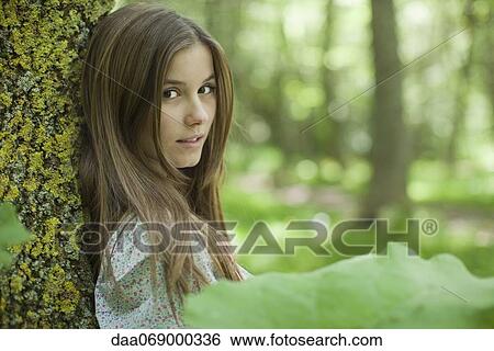 Young woman leaning against tree in woods View Large Photo Image Stock Photograph - Young woman leaning against tree in woods. Fotosearch
