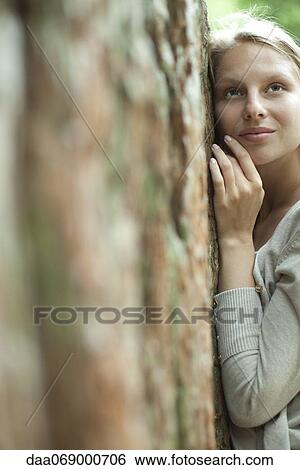 Stock Photograph - Young woman leaning against tree. Fotosearch