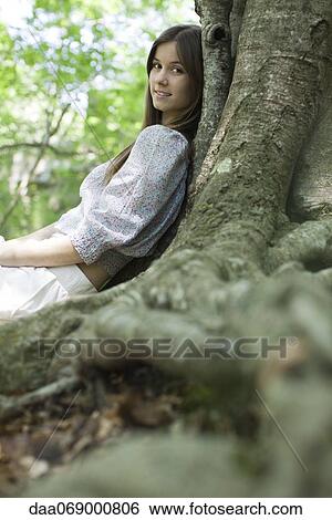 Stock Photograph - Young woman leaning against tree. Fotosearch