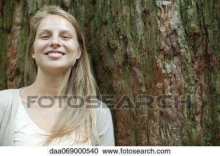 Young woman leaning against tree trunk, portrait View Large Photo Image Stock Image - Young woman leaning against tree trunk, portrait. Fotosearch