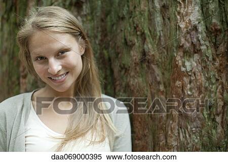 Young woman leaning against tree trunk, portrait View Large Photo Image Stock Photography - Young woman leaning against tree trunk, portrait. Fotosearch