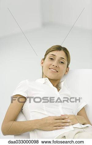 Stock Photo - Young woman leaning back in chair, smiling at camera. Fotosearch