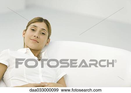 Stock Photo - Young woman leaning back in chair, smiling at camera. Fotosearch
