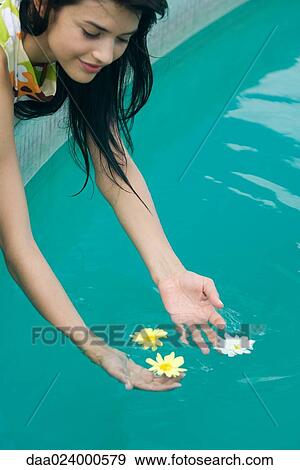 Young woman leaning over to pick up flowers floating in swimming pool, cropped view View Large Photo Image Stock Photo - Young woman leaning over to pick up flowers floating in swimming pool, cropped view. Fotosearch