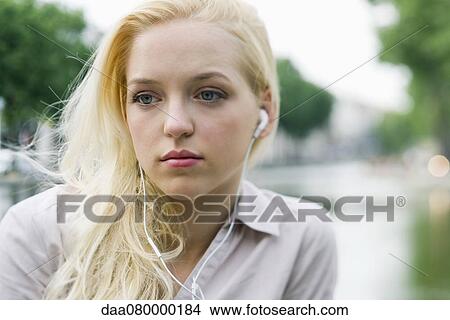 Picture - Young woman listening to earphones, looking away in thought. Fotosearch