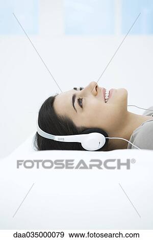 Stock Photo - Young woman listening to headphones, looking up, smiling. Fotosearch
