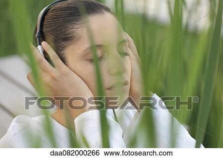 Stock Photograph - Young woman listening to headphones outdoors with eyes closed. Fotosearch