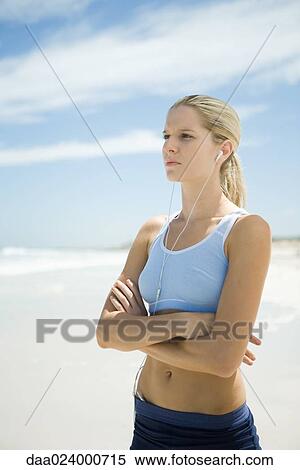 Stock Photography - Young woman listening to MP3 player on beach, looking away. Fotosearch