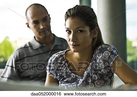 Stock Photograph - Young woman looking at camera, husband in background. Fotosearch