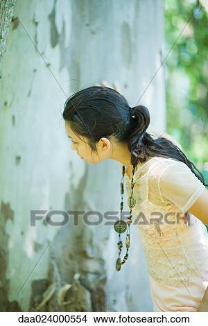 Young woman looking at tree trunk, side view View Large Photo Image Picture - Young woman looking at tree trunk, side view. Fotosearch