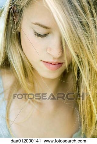 Stock Image - Young woman looking down, hair covering one eye, portrait. Fotosearch