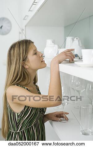 Young woman looking for dish stored on shelf View Large Photo Image Stock Photo - Young woman looking for dish stored on shelf. Fotosearch