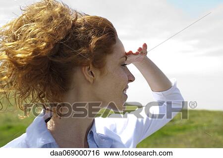 Stock Photograph - Young woman looking into distance, hand shading eyes. Fotosearch