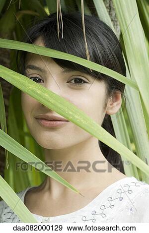 Young woman looking through foliage, portrait View Large Photo Image Stock Photo - Young woman looking through foliage, portrait. Fotosearch