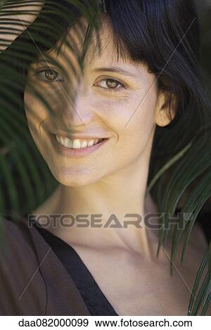 Young woman looking through palm leaf, smiling, portrait View Large Photo Image Stock Photo - Young woman looking through palm leaf, smiling, portrait. Fotosearch